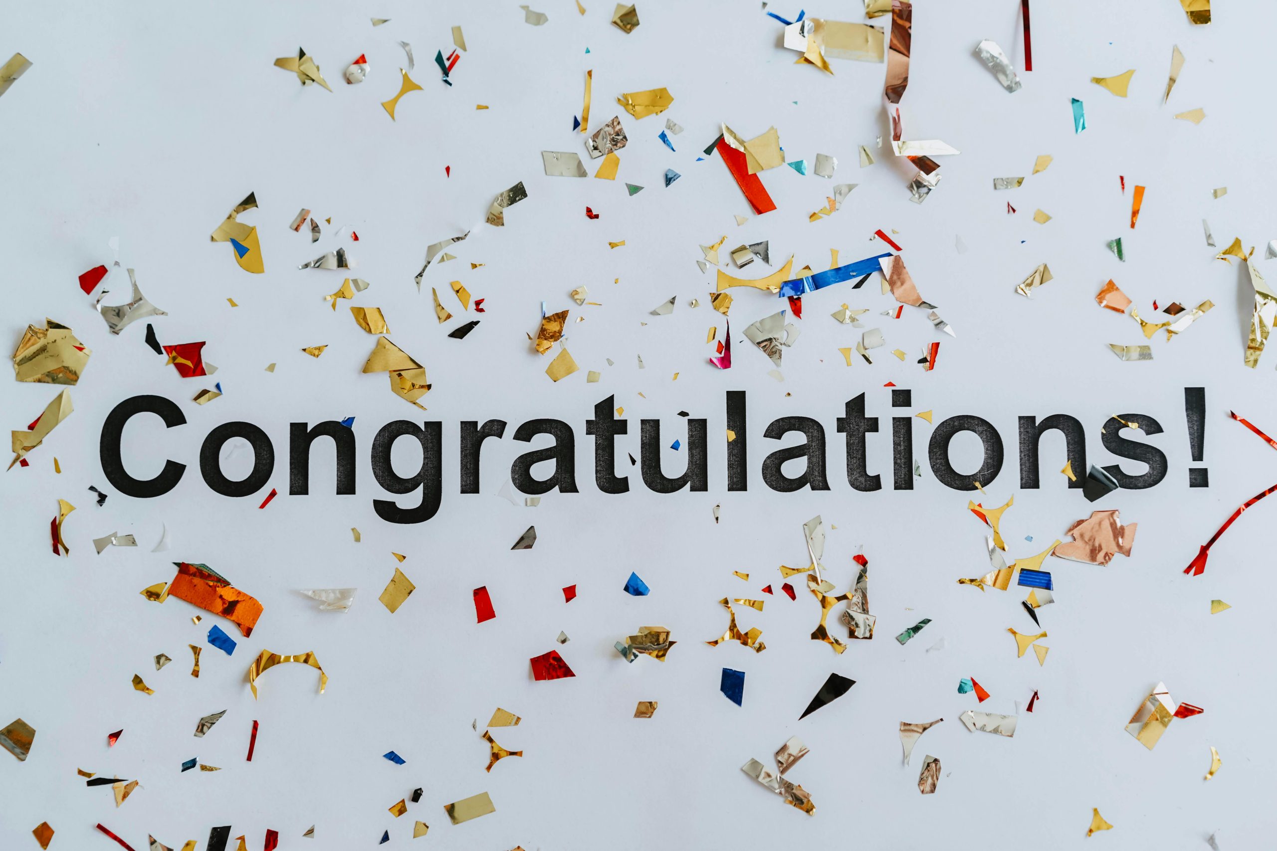 A vibrant congratulatory image with colorful confetti scattered around the word 'Congratulations!' on a white surface.